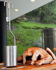 accesorio para pollo sobre tabla de madera y al lado un poco sazonado en paprika con un barril asador de fondo