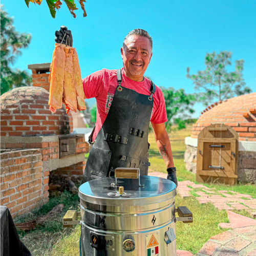 Hombre con delantal junto al barril asador Humo Barriles de 13 Kg encendido al aire libre